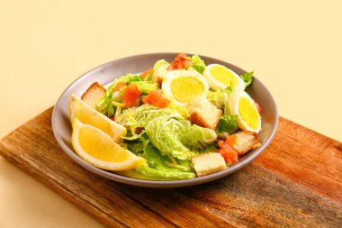 Board with plate of delicious salad on beige background