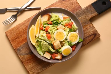 Board with plate of delicious salad on beige background