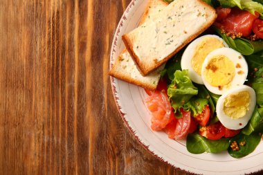 Plate of delicious salad with boiled eggs and salmon on brown wooden background