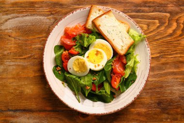 Plate of delicious salad with boiled eggs and salmon on brown wooden background