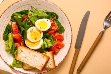 Plate of delicious salad with boiled eggs and salmon on beige background
