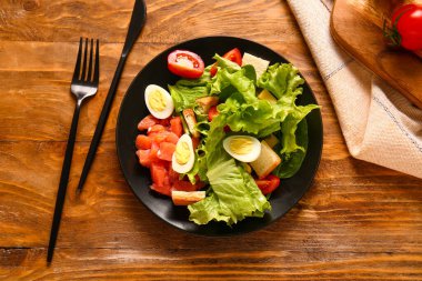 Plate of delicious salad with boiled eggs and salmon on brown wooden background
