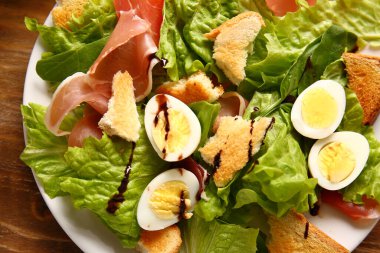 Plate of delicious salad with boiled eggs and jamon on brown wooden background