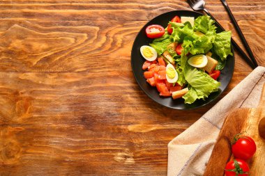 Plate of delicious salad with boiled eggs and salmon on brown wooden background