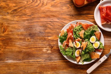 Plate of delicious salad with boiled eggs and jamon on brown wooden background