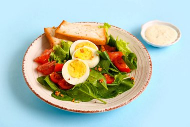 Plate of delicious salad with boiled eggs and salmon on blue background