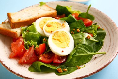 Plate of delicious salad with boiled eggs and salmon on blue background