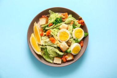 Plate of delicious salad with boiled eggs and salmon on blue background