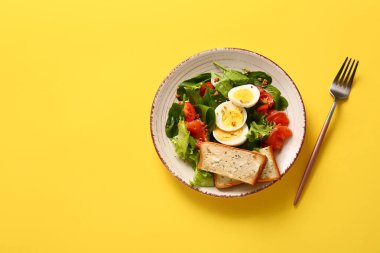 Plate of delicious salad with boiled eggs and salmon on yellow background