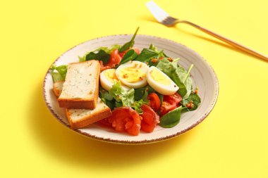 Plate of delicious salad with boiled eggs and salmon on yellow background