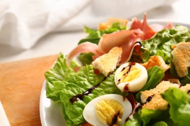 Plate of delicious salad with boiled eggs and jamon on wooden board, closeup
