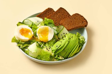 Plate of delicious salad with boiled eggs and avocado on beige background
