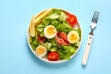 Plate of delicious salad with boiled eggs and jamon on blue background