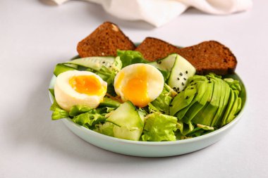 Plate of delicious salad with boiled eggs and avocado on grey background