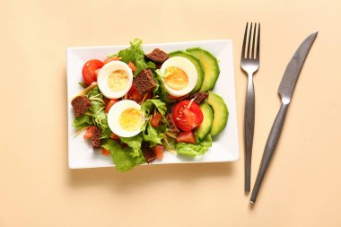 Plate of delicious salad with boiled eggs and salmon on beige background