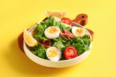 Board with plate of delicious salad on yellow background