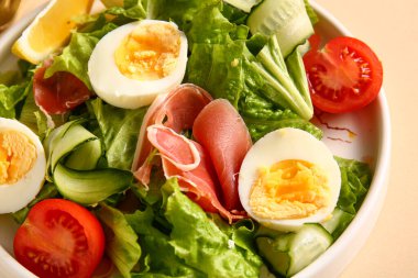 Plate of delicious salad with boiled eggs and jamon on beige background, closeup