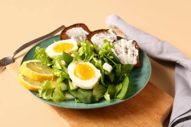 Plate of delicious salad with boiled eggs and cream cheese sandwiches on beige background