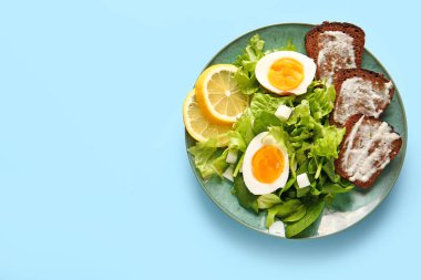 Plate of delicious salad with boiled eggs and cream cheese sandwiches on blue background