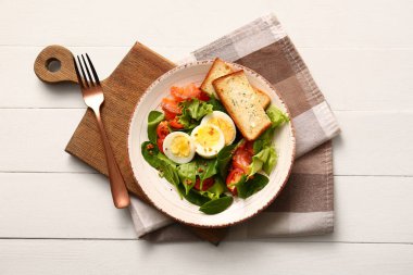 Plate of delicious salad with boiled eggs and salmon on white wooden background