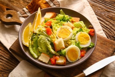 Plate of delicious salad with boiled eggs and salmon on brown wooden background