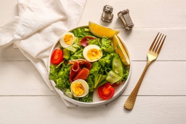 Plate of delicious salad with boiled eggs and jamon on white wooden background