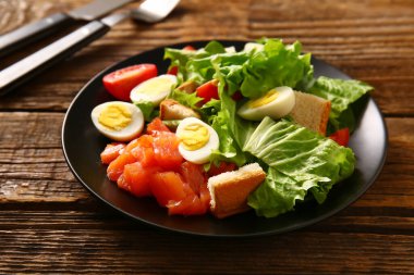 Plate of delicious salad with boiled eggs and salmon on brown wooden background