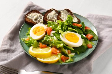 Plate of delicious salad with boiled eggs and salmon on white wooden background