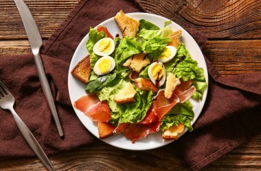 Plate of delicious salad with boiled eggs and jamon on brown wooden background