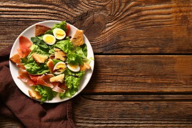 Plate of delicious salad with boiled eggs and jamon on brown wooden background