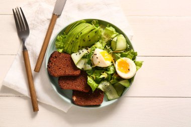 Plate of delicious salad with boiled eggs and avocado on white wooden background