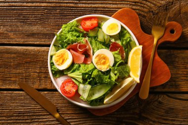 Plate of delicious salad with boiled eggs and jamon on brown wooden background