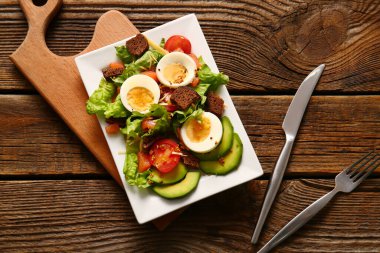 Plate of delicious salad with boiled eggs and salmon on brown wooden background