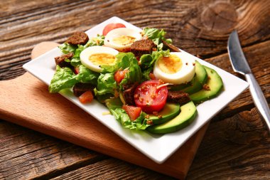 Plate of delicious salad with boiled eggs and salmon on brown wooden background
