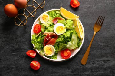 Plate of delicious salad with boiled eggs and jamon on black grunge background