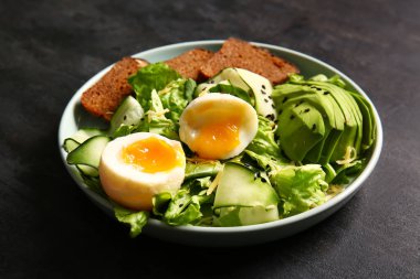 Plate of delicious salad with boiled eggs and avocado on black grunge background