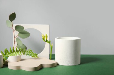 Plaster podiums and different plants on green table against grey background