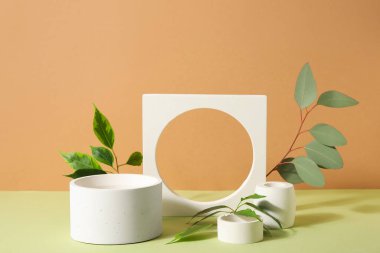 Plaster podiums with eucalyptus and ficus branches on green table against brown background