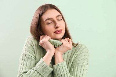 Pretty stylish young woman in warm knitted sweater on mint background