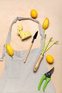 Gardener's tools with Easter eggs, rabbit and tulips on beige background