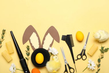 Hairdresser's accessories with Easter eggs, paper bunny ears, flowers and chickens on yellow background
