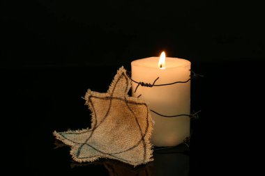 Burning candle with barbed wire and Jewish badge on dark background. International Holocaust Remembrance Day