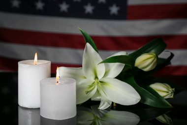 Burning candles with lilies on table against USA flag. National Day of Prayer and Remembrance for the Victims of the Terrorist Attacks