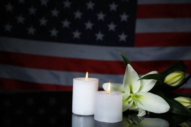 Burning candles with lilies on table against USA flag. National Day of Prayer and Remembrance for the Victims of the Terrorist Attacks