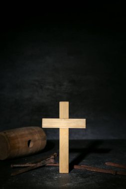 Wooden cross with nails and mallet on dark background, closeup. Good Friday concept