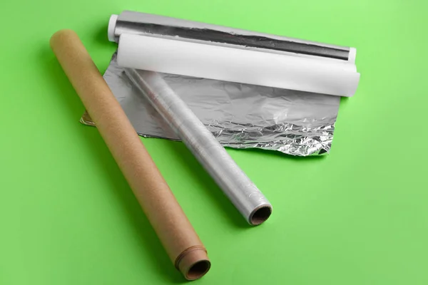 Rolls of aluminium foil, baking paper and food film on green background