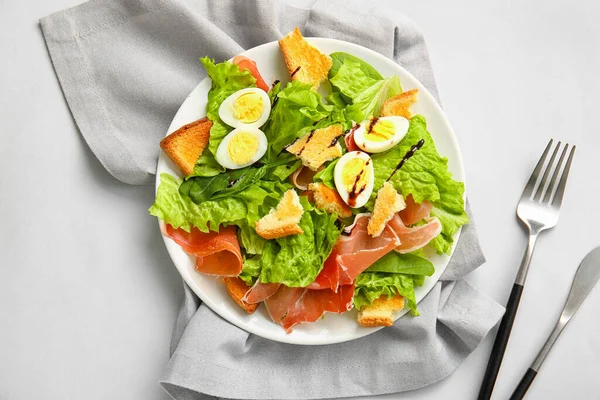Plate of delicious salad with boiled  eggs and jamon on grey background