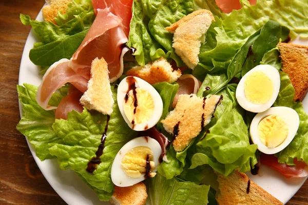 Plate of delicious salad with boiled eggs and jamon on brown wooden background
