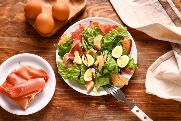 Plate of delicious salad with boiled eggs and jamon on brown wooden background