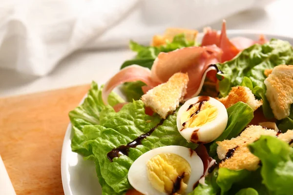 Plate of delicious salad with boiled eggs and jamon on wooden board, closeup